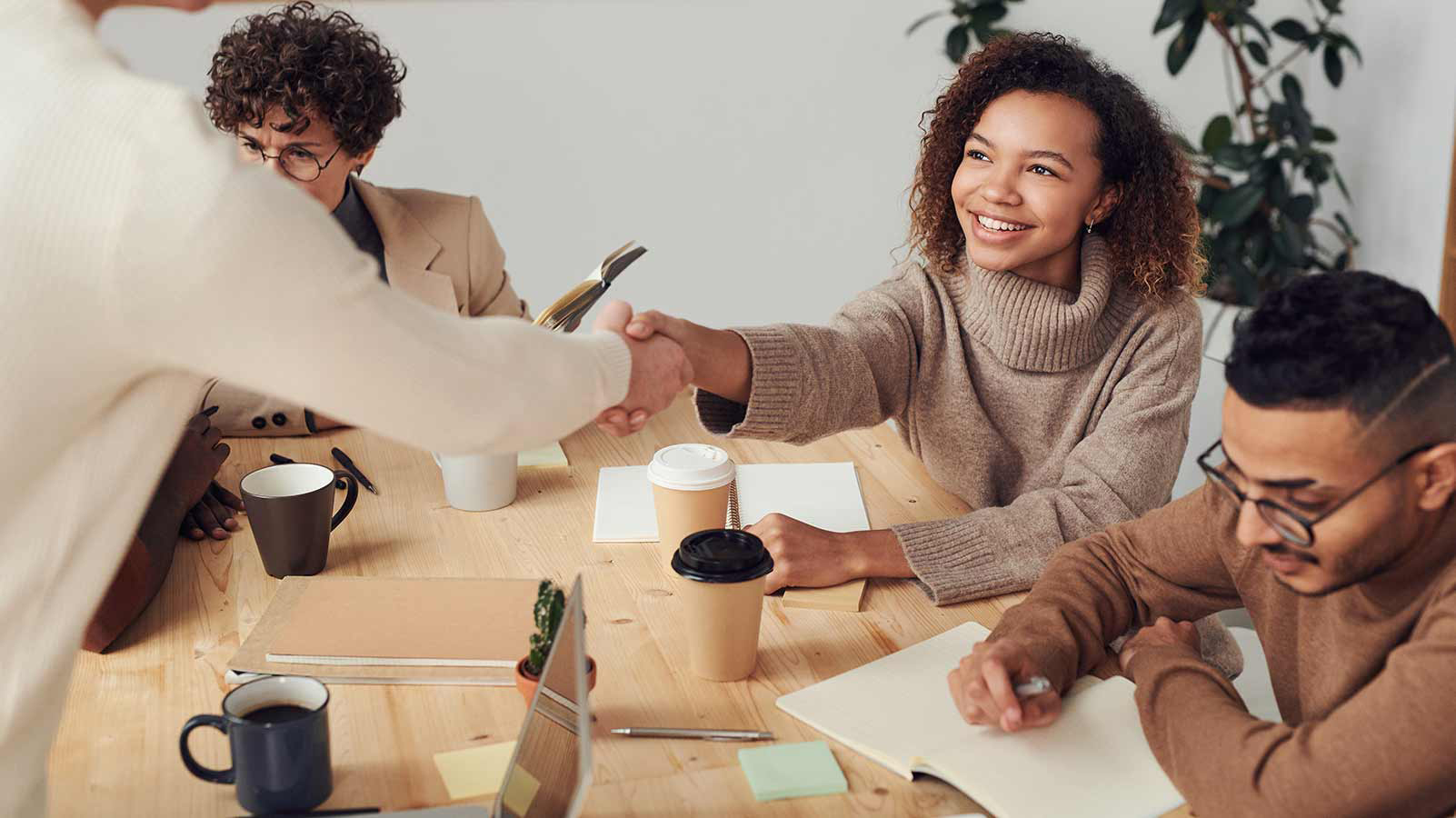  A diverse group of individuals collaborates around a table, engaging with a laptop in a productive meeting setting.