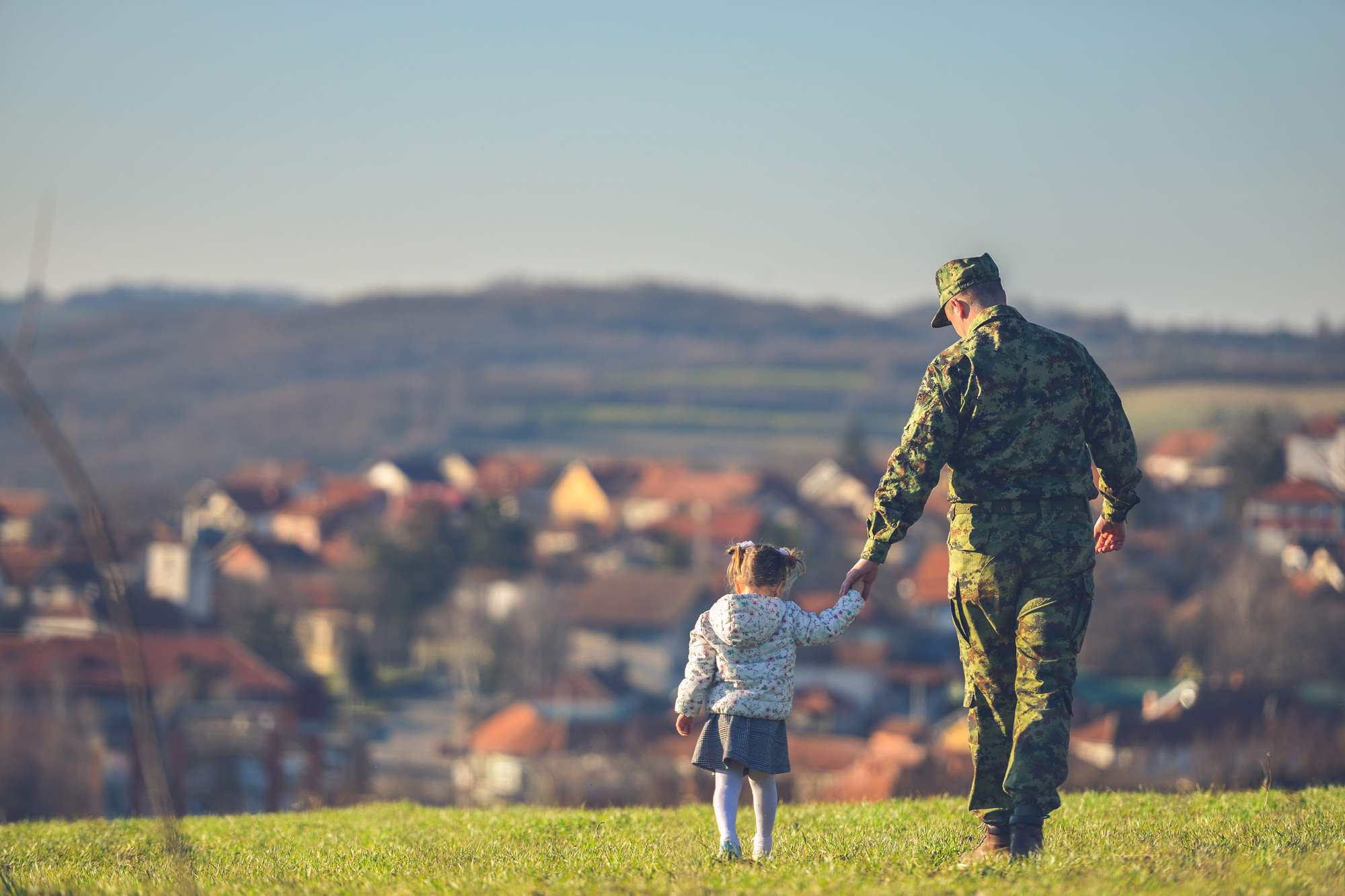 Man and child walking in a field toward a town.
